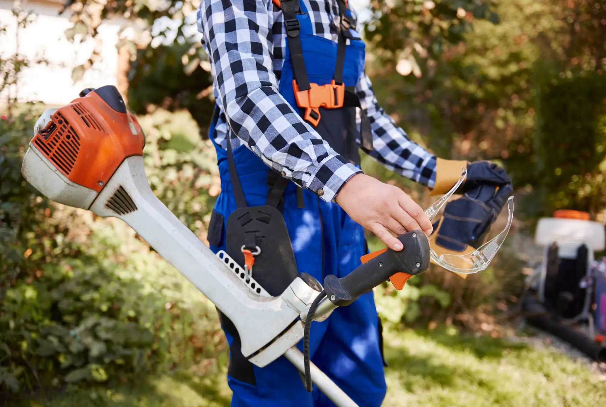 A gardener with PPE, cutting and shaping shrubs using a cutter