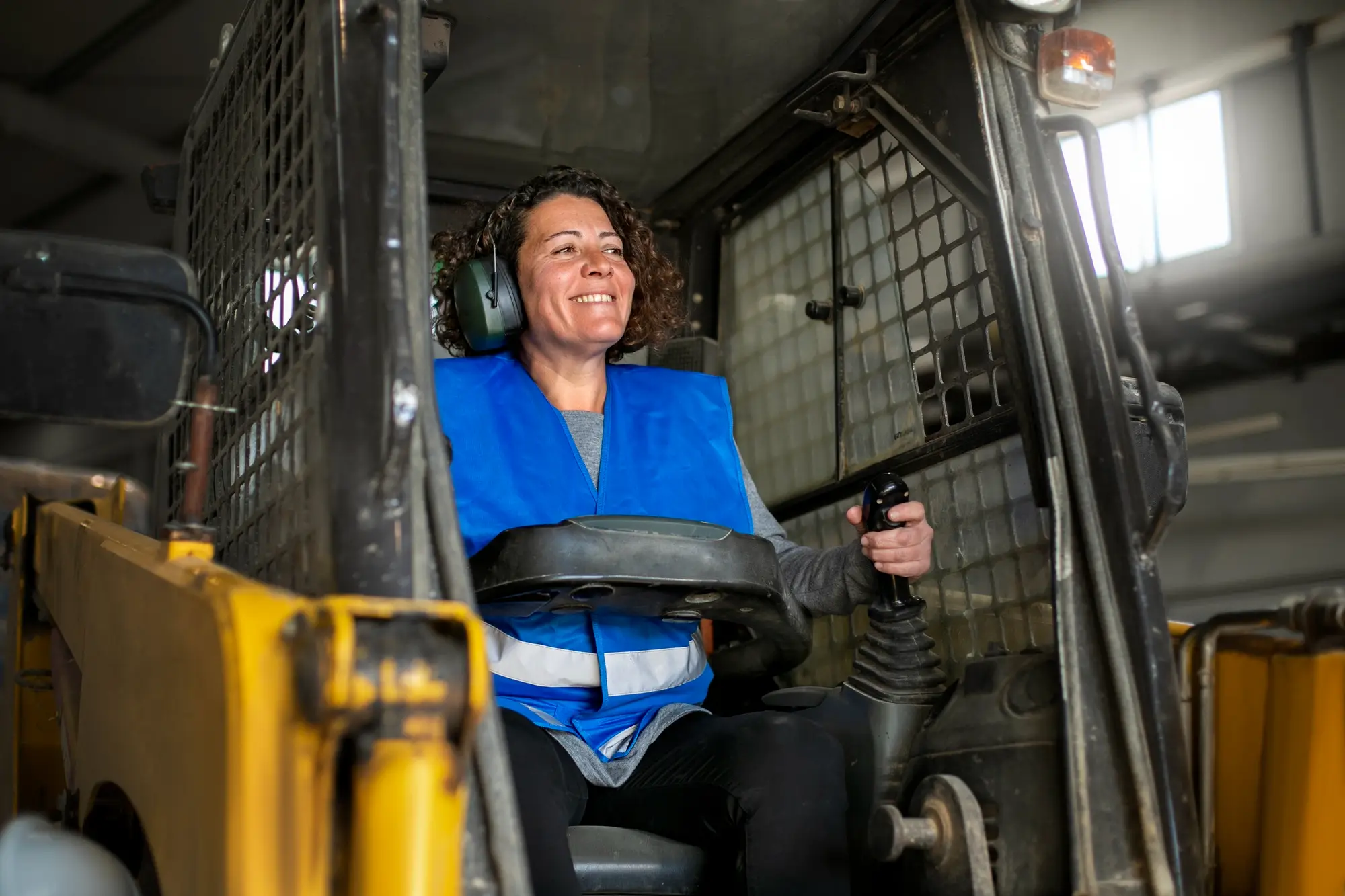 A female operator with headphones for clear communication, while operating Skid Steer Loader